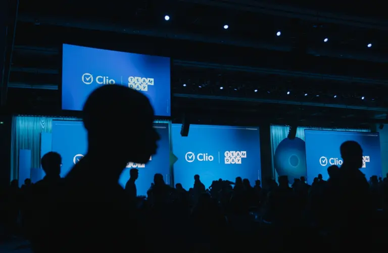 Silhouettes of people in front of large blue screens displaying "Clio Team Day" at an event.