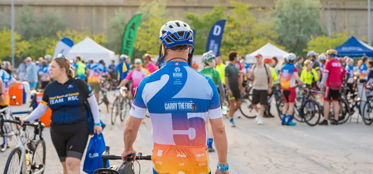 A group of cyclists gathered for an outdoor event with tents and banners in the background.
