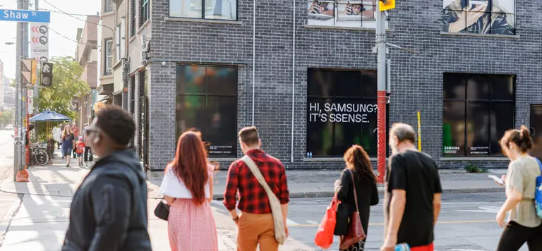 Des personnes traversant une rue devant un bâtiment en briques avec des affiches et des publicités.