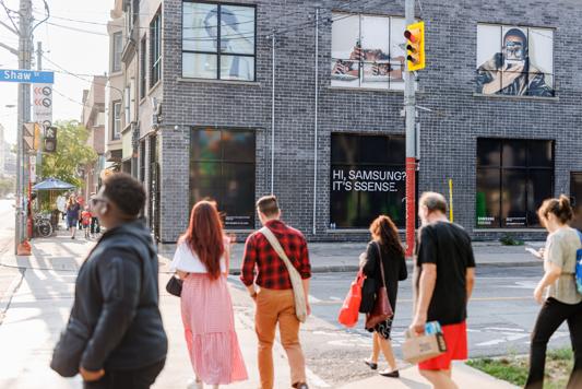 Des personnes traversant une rue devant un bâtiment en briques avec des affiches et des publicités.