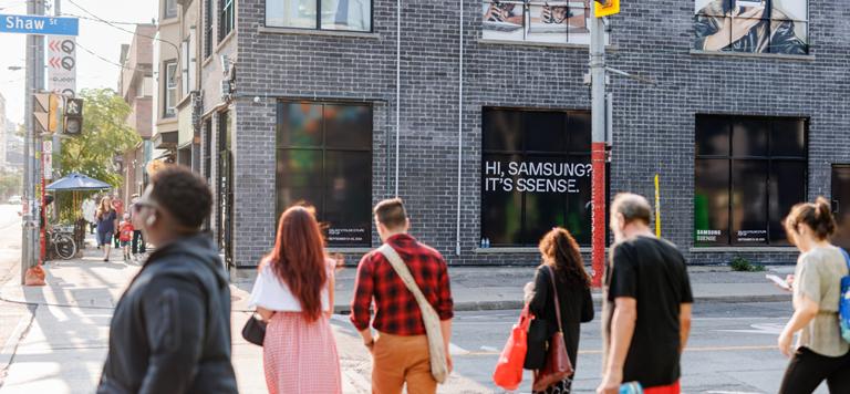 Des personnes traversant une rue devant un bâtiment en briques avec des affiches et des publicités.