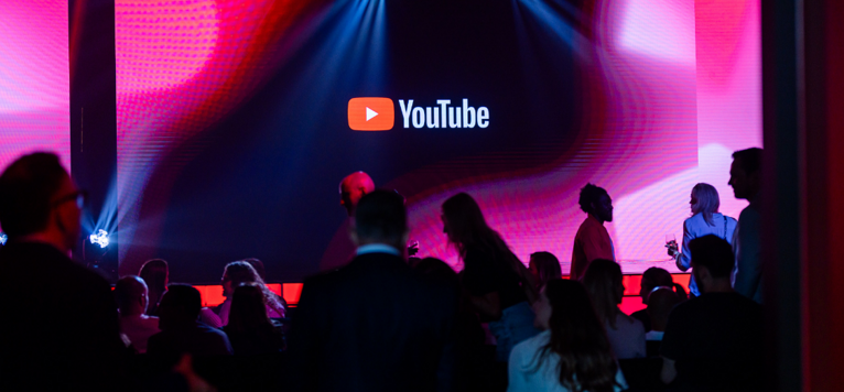 Public dans une salle faiblement éclairée regardant un grand écran avec le logo YouTube.