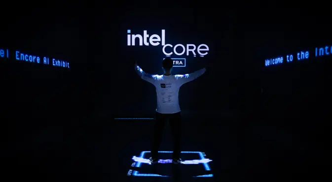 Une personne se tient les bras tendus devant une enseigne Intel Core illuminée dans une pièce sombre.