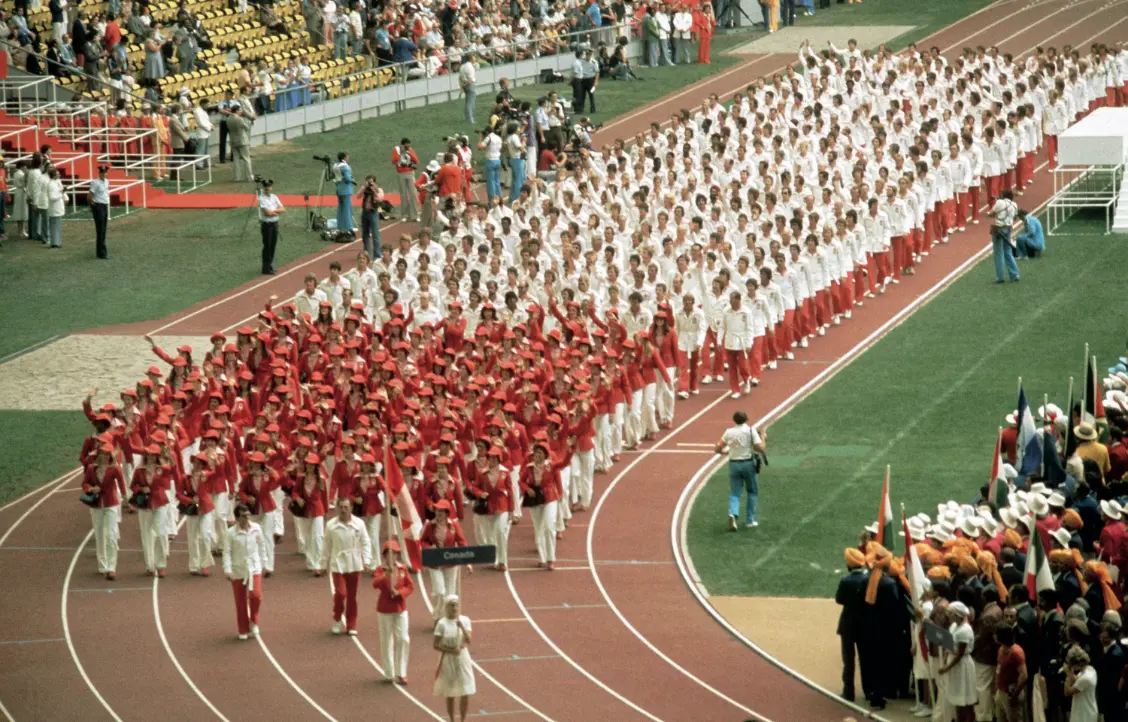 Un grand groupe d'athlètes en uniformes rouges et blancs défilent ensemble dans un stade lors d'une cérémonie d'ouverture.