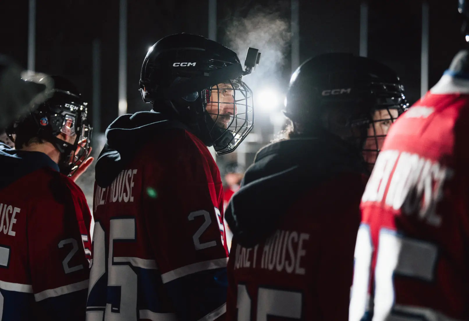 Des joueurs de hockey portant des maillots rouges et des casques se tiennent sur la glace, avec une respiration visible dans l'air froid.