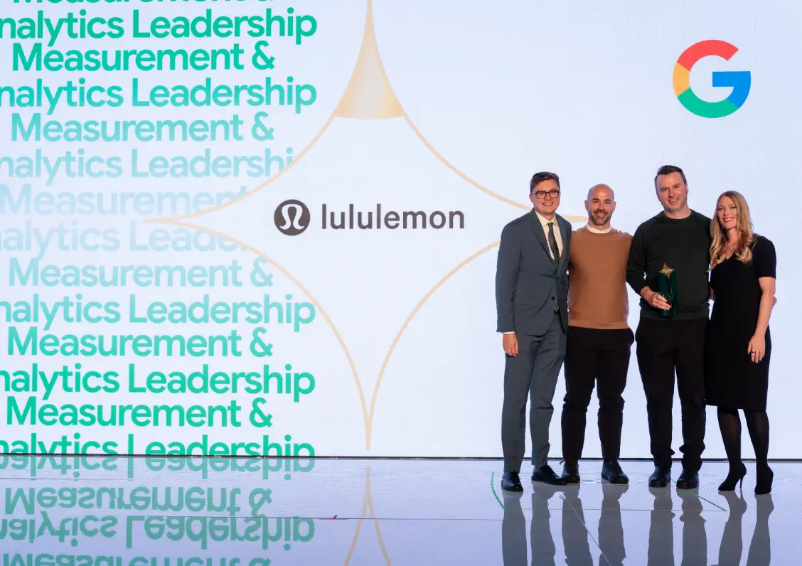 Quatre personnes posent sur scène avec un logo Lululemon et un symbole Google sur un grand écran derrière elles.
