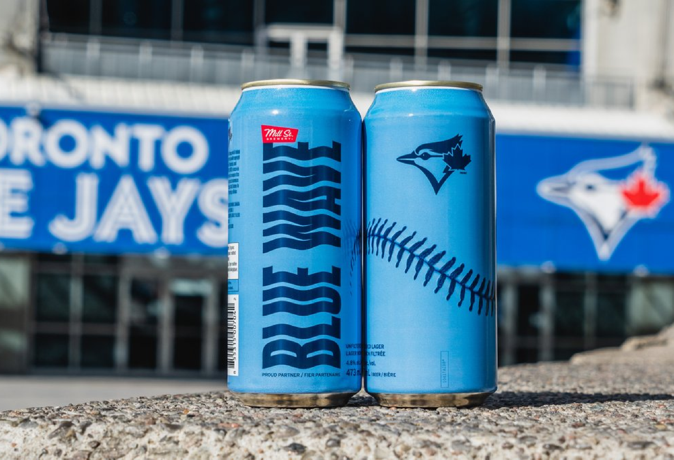 Deux canettes bleues avec un design sur le thème du baseball devant un panneau des Blue Jays de Toronto.