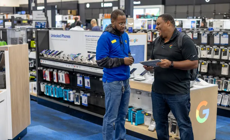 Deux hommes parlent et regardent une tablette dans un magasin d'électronique.