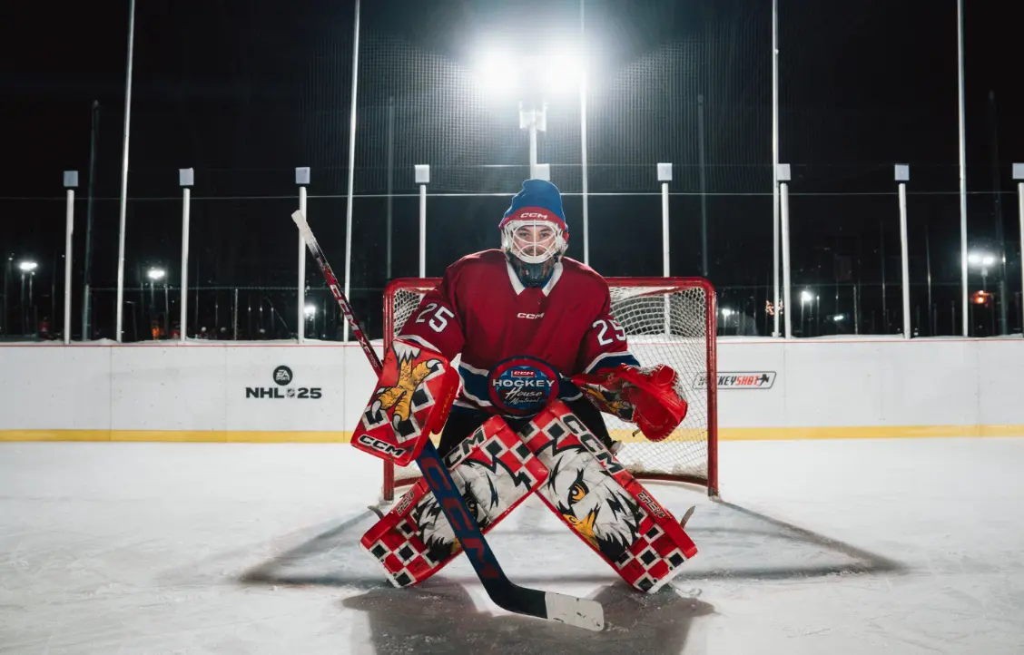 Un gardien de but de hockey en équipement complet se tient devant le filet sur une patinoire extérieure la nuit.