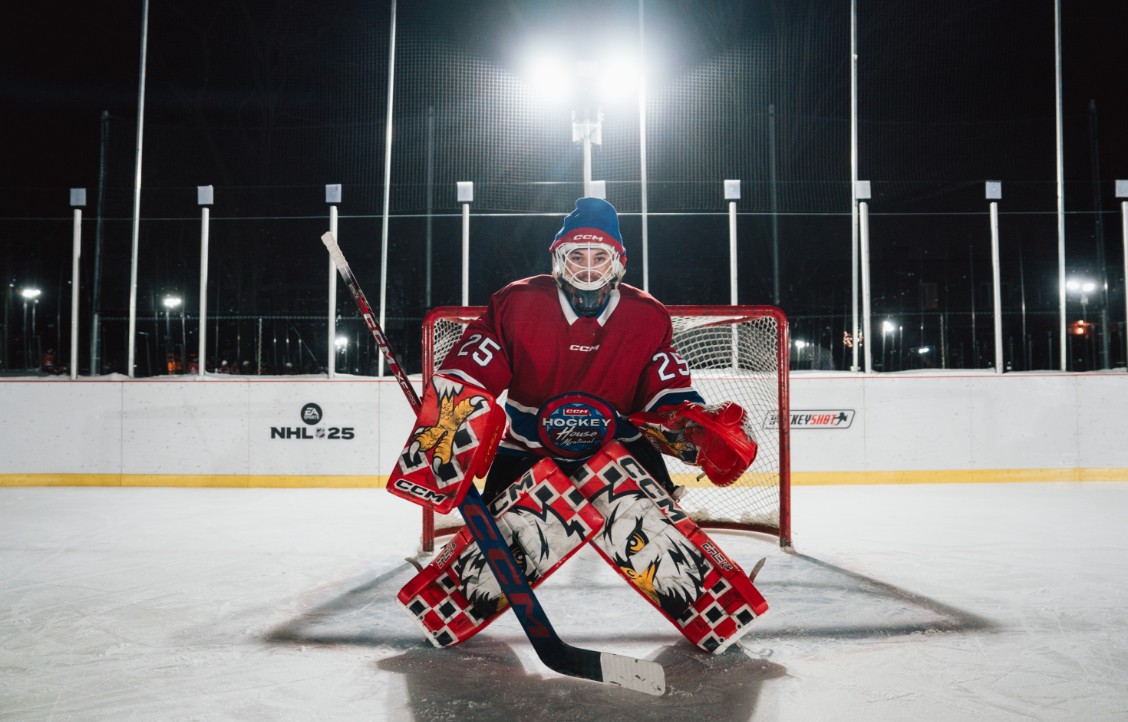 Un gardien de but de hockey en équipement complet se tient devant le filet sur une patinoire extérieure la nuit.