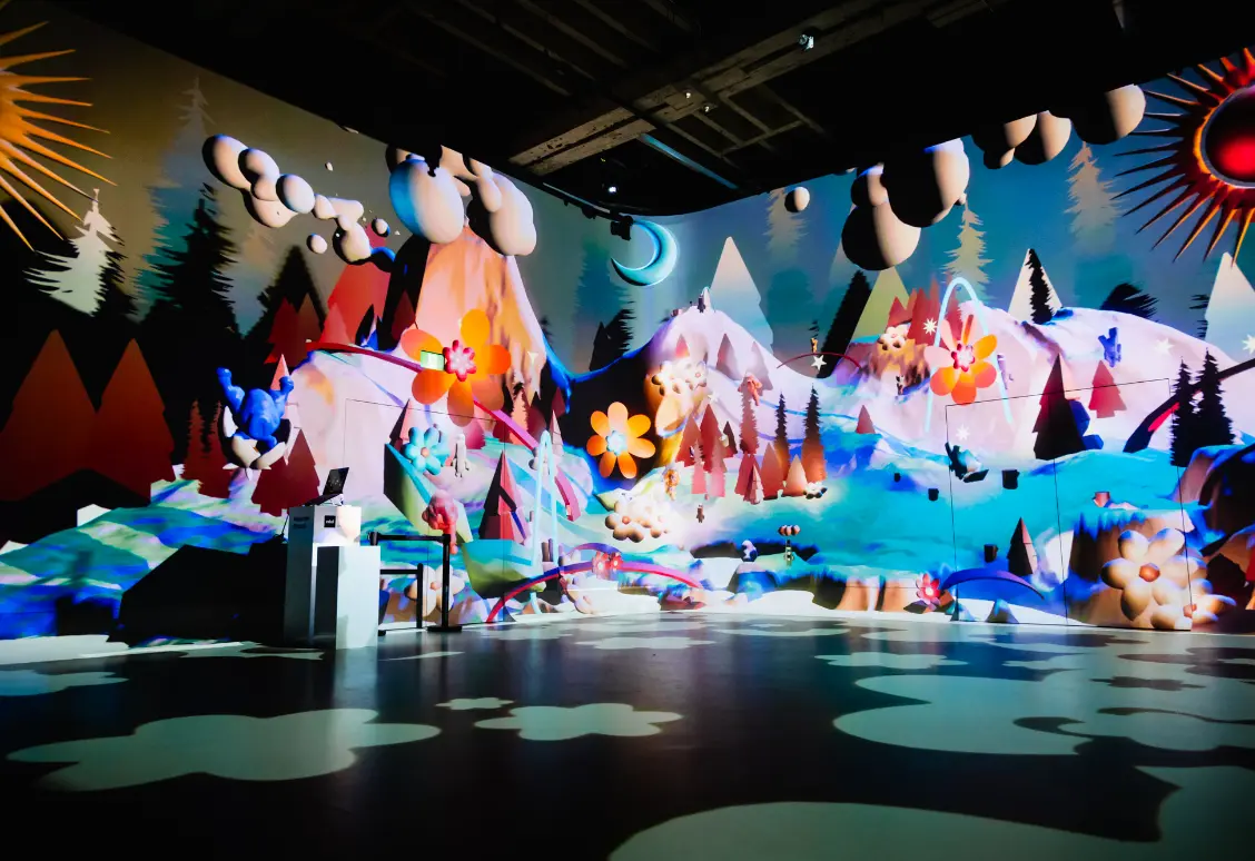 Une installation artistique colorée et fantaisiste présentant des montagnes, des fleurs et des arbres avec une atmosphère ludique et onirique.