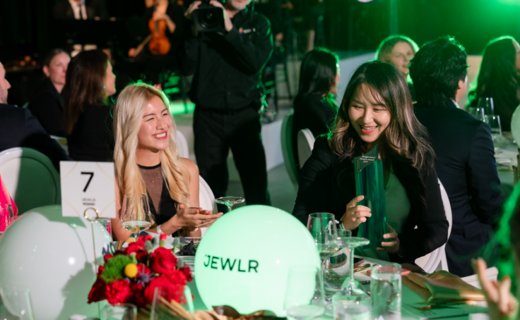 Deux femmes souriant et discutant lors d'un dîner formel avec un éclairage vert.