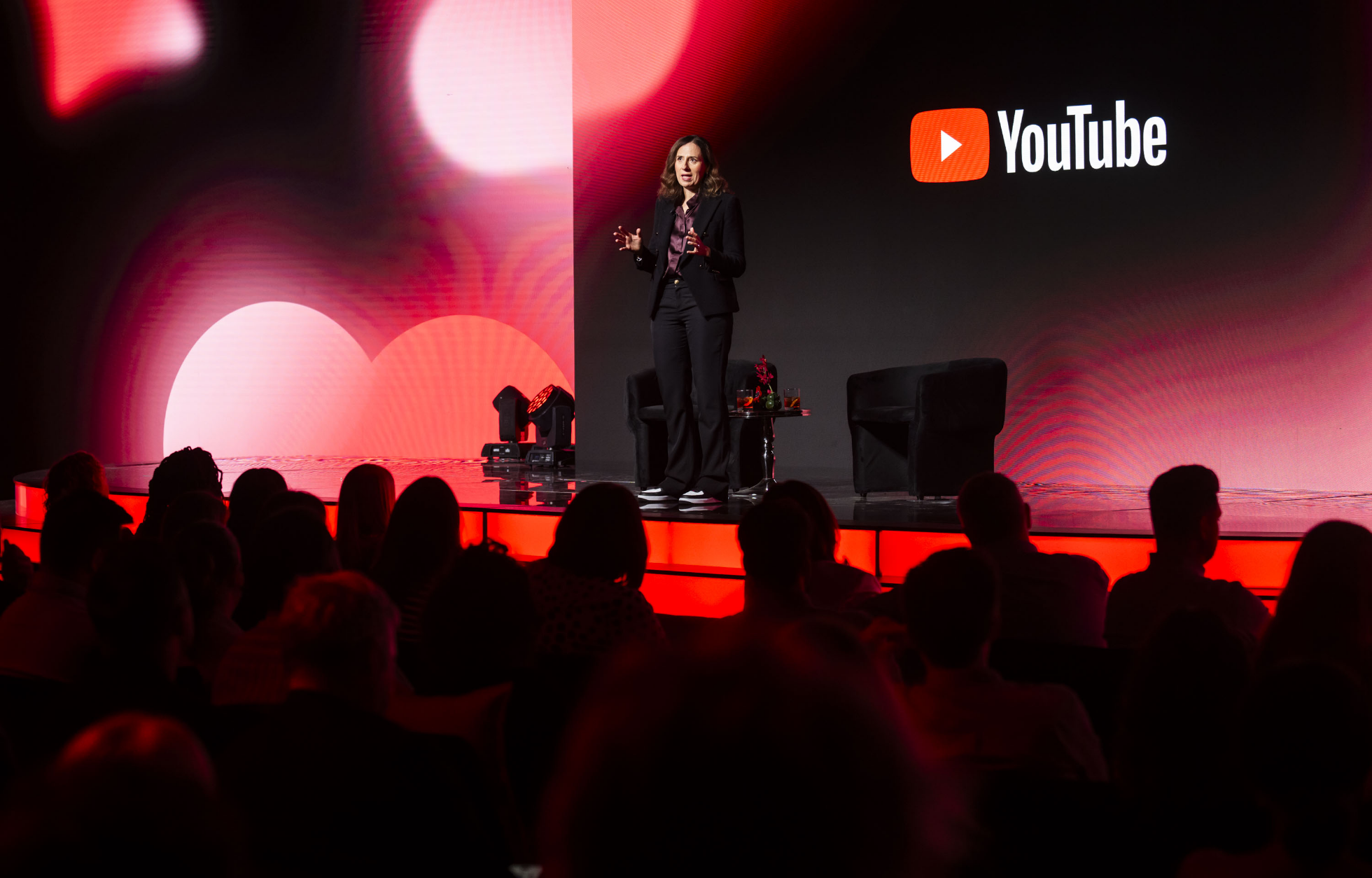 Une personne se tient sur une scène devant un public, avec le logo YouTube affiché sur un grand écran en arrière-plan.