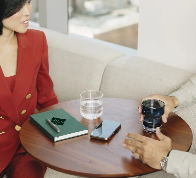 Deux personnes assises à une petite table ronde avec un carnet, un smartphone et des verres d'eau.