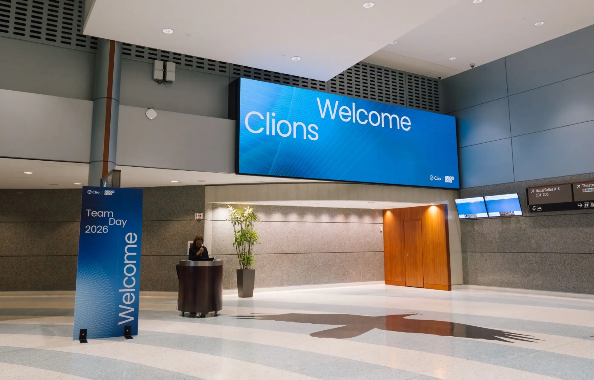 Un hall spacieux avec une bannière qui dit "Welcome Clions" et un panneau qui dit "Team Day 2026 Welcome."