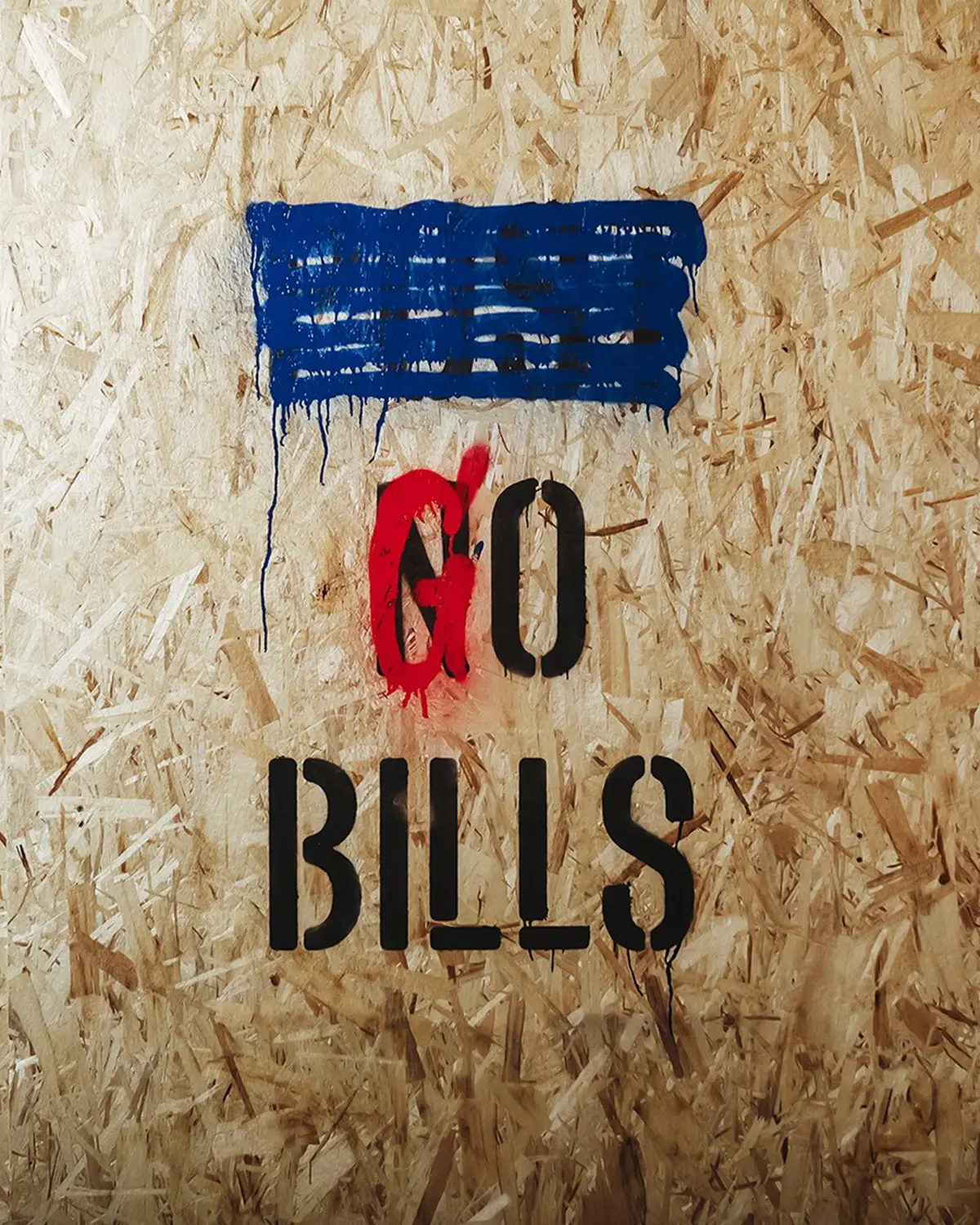 Le texte "GO BILLS" est peint au pochoir sur une surface de bois texturée avec des gouttes de peinture bleue et rouge au-dessus.