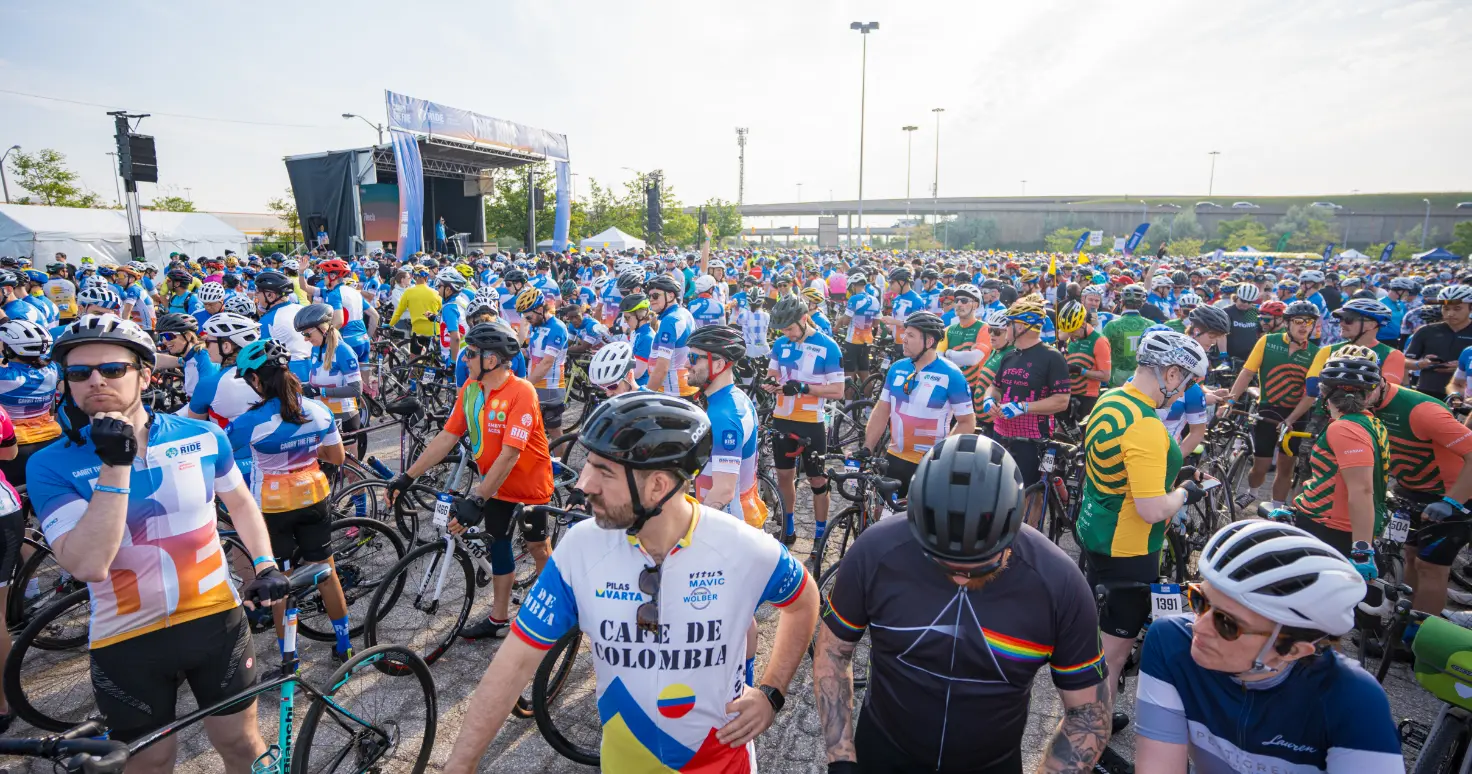 A large group of cyclists gathers at the starting line of a race, wearing colorful jerseys and helmets.