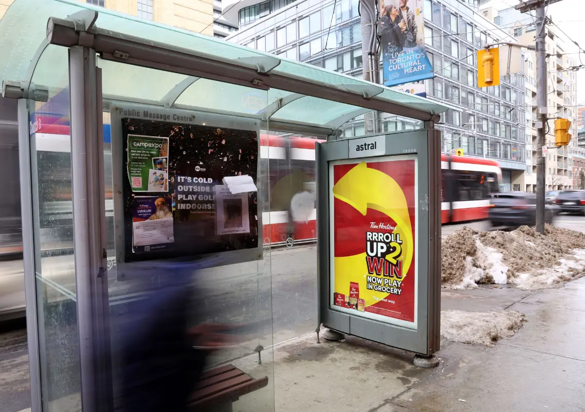 Un arrêt de bus urbain avec des publicités et un tramway qui passe, sur fond de bâtiments urbains.
