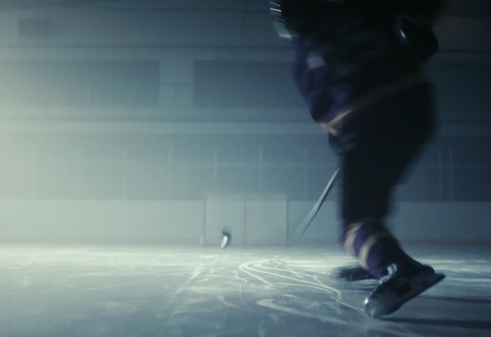 A hockey player skates on an ice rink, with a puck flying through the air towards a goal.