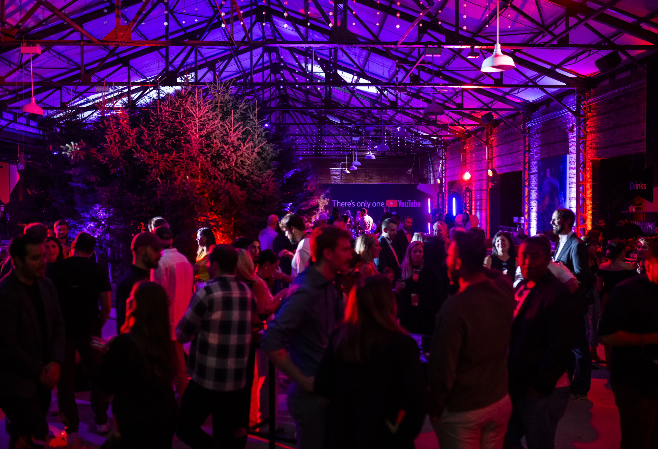 Une fête intérieure animée avec un éclairage coloré, présentant une foule de personnes socialisant sous un haut plafond.