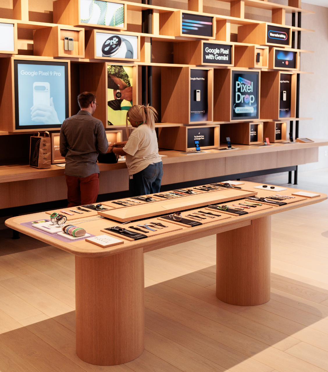 Un intérieur de magasin de détail moderne avec des gadgets technologiques exposés sur des tables et des étagères, et deux personnes interagissant près d'un comptoir.