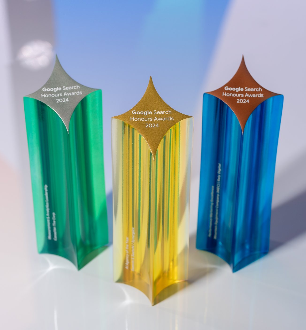 Trois trophées colorés en forme d'étoile étiquetés « Google Search Honours Awards 2024 » en vert, jaune et bleu.