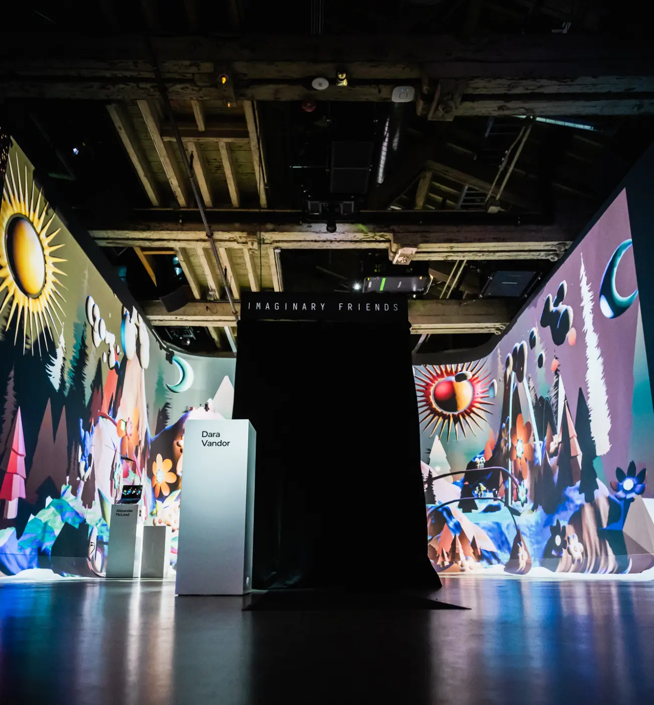 Une pièce faiblement éclairée avec des fresques murales abstraites colorées présentant une installation sombre centrale étiquetée « Imaginary Friends ».