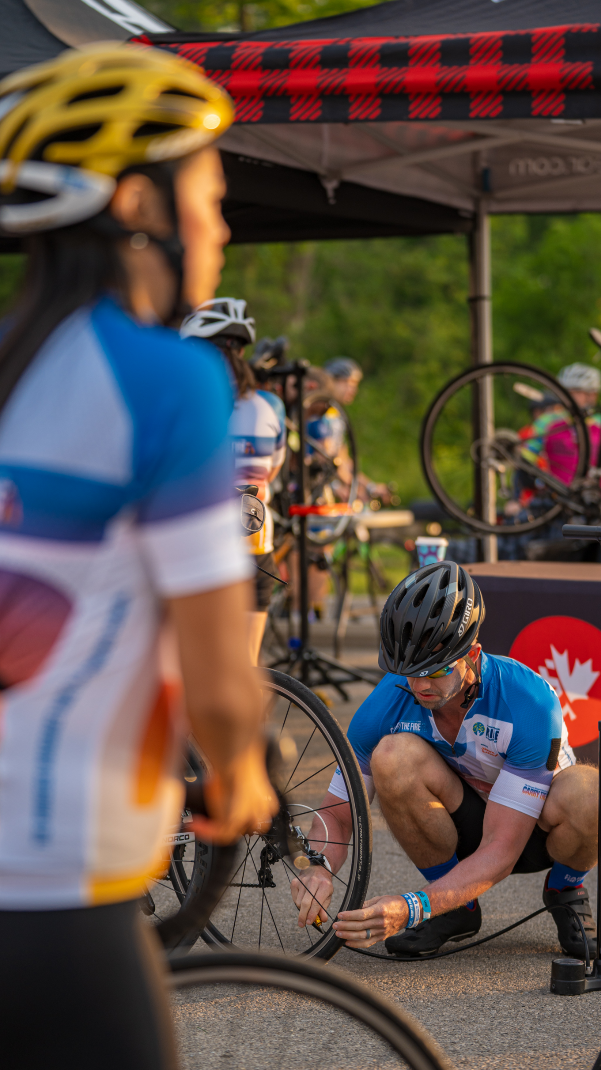 Un groupe de cyclistes en casques et maillots se rassemble près d'une tente, avec une personne réparant un pneu de vélo.