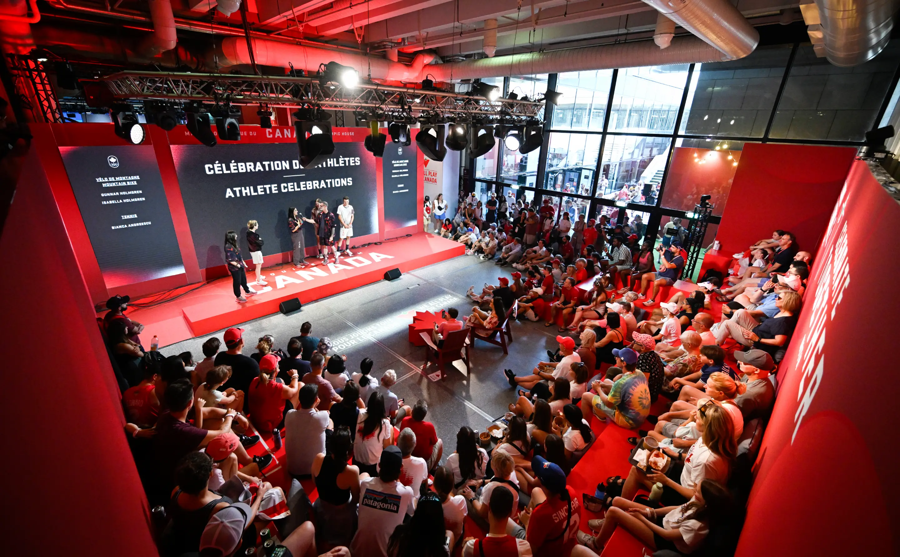 Une grande foule se rassemble dans une salle à thème rouge regardant une présentation sur scène célébrant les athlètes.