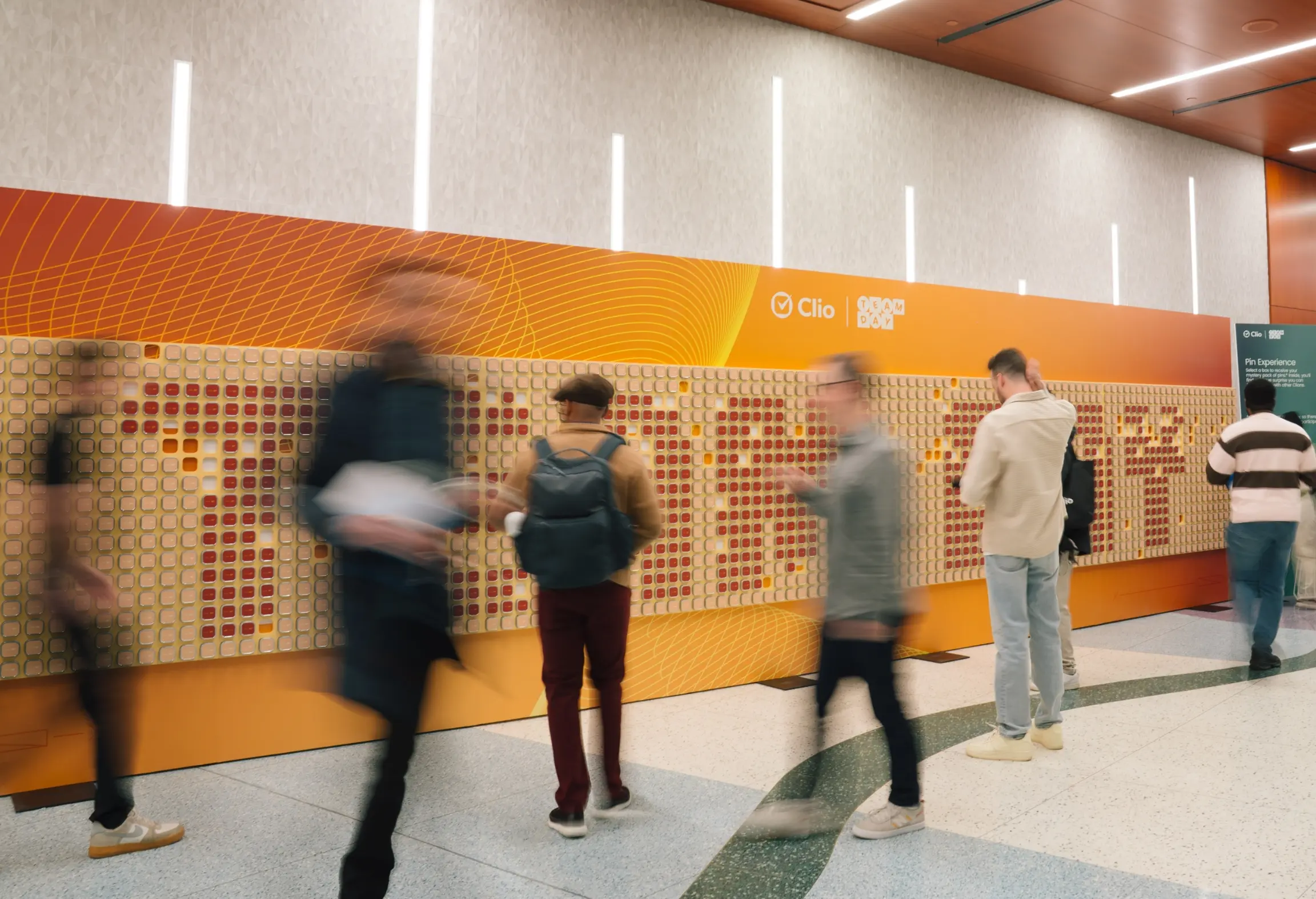 Des personnes interagissant avec un grand mur d'affichage couvert de carreaux carrés avec un design coloré dans un cadre moderne.