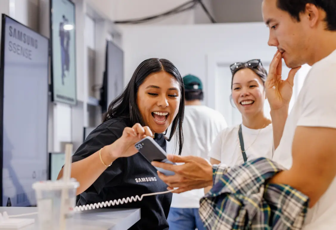 Un employé de Samsung montre un téléphone à deux clients souriants dans un magasin.