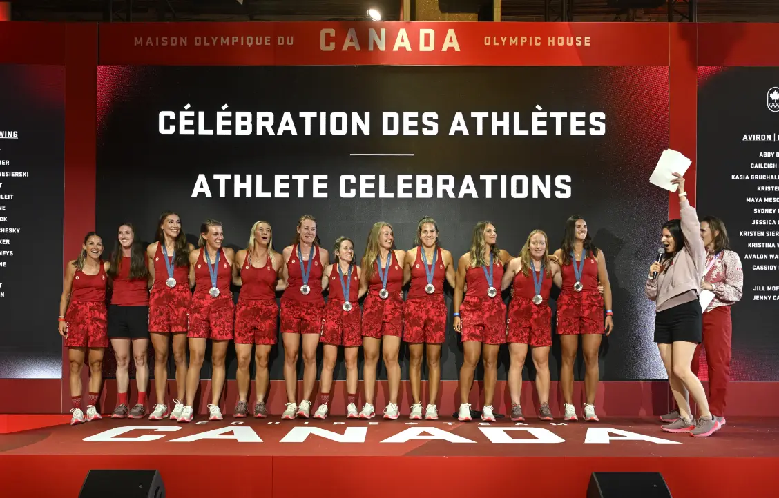 Un groupe d'athlètes portant des médailles se tient sur une scène sous un panneau qui dit « Célébrations d'athlètes » en français et en anglais.