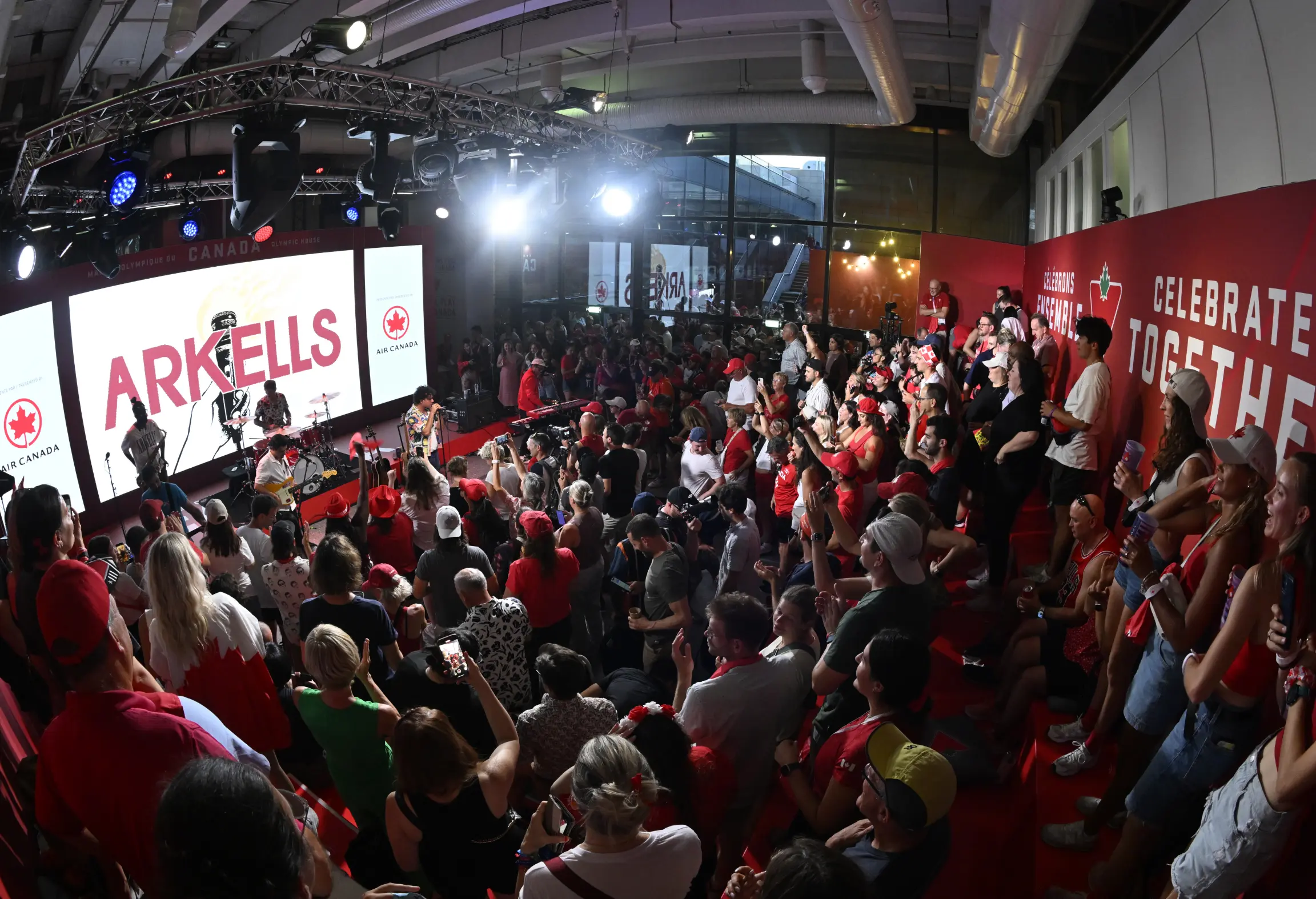Un groupe se produit sur scène devant une grande foule enthousiaste à l'intérieur d'une salle.