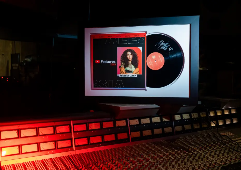 Un disque vinyle encadré et une photo sont affichés au-dessus d'une console de mixage audio.