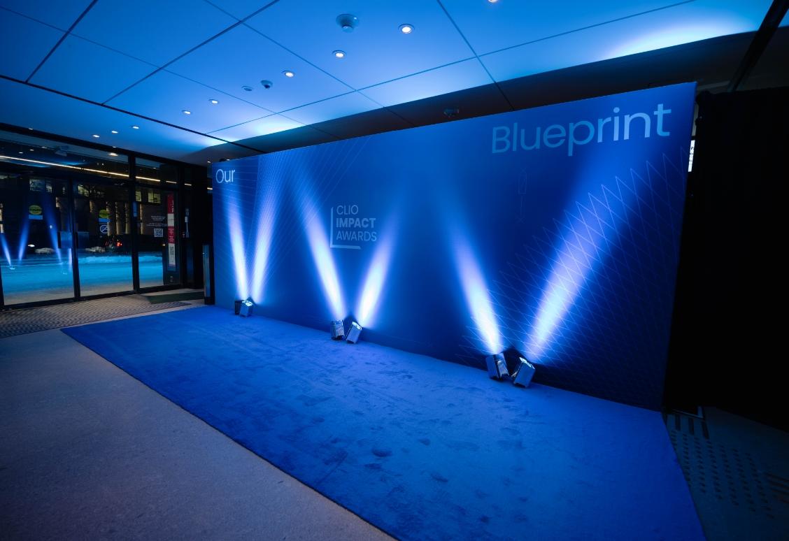 Un espace événementiel sur le thème bleu avec la toile de fond "Clio Impact Awards" et des projecteurs.