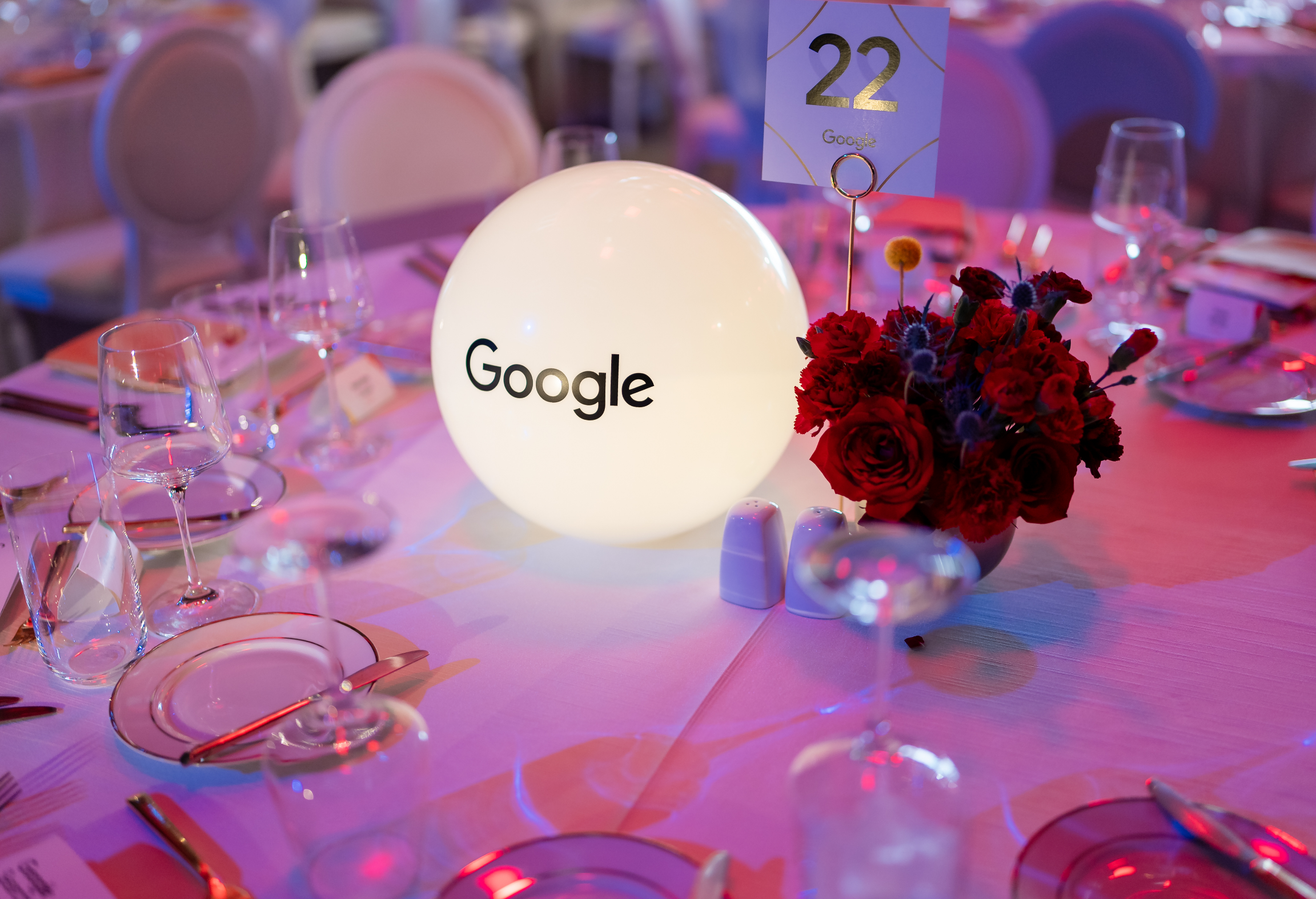 Une table d'événement décorée avec une sphère lumineuse étiquetée « Google », un bouquet de fleurs rouges et le numéro de table 22.