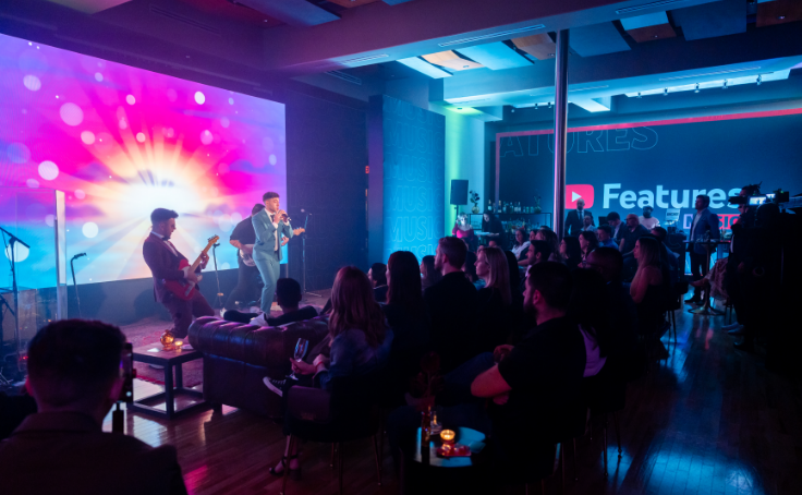 Un groupe live se produit sur une scène avec des lumières colorées devant un public dans une salle intérieure.