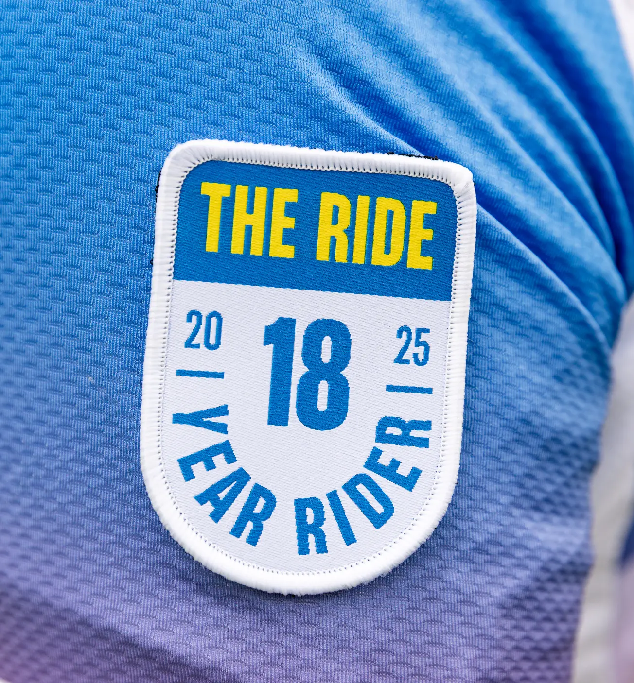 A patch on a blue shirt reads "The Ride, 2025, 18 Year Rider."