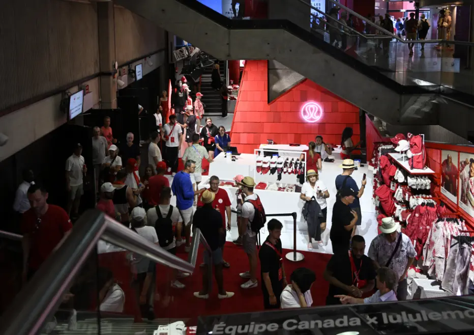 Un magasin animé avec des personnes faisant leurs achats de marchandises sportives, présentant des vêtements rouges et blancs exposés.