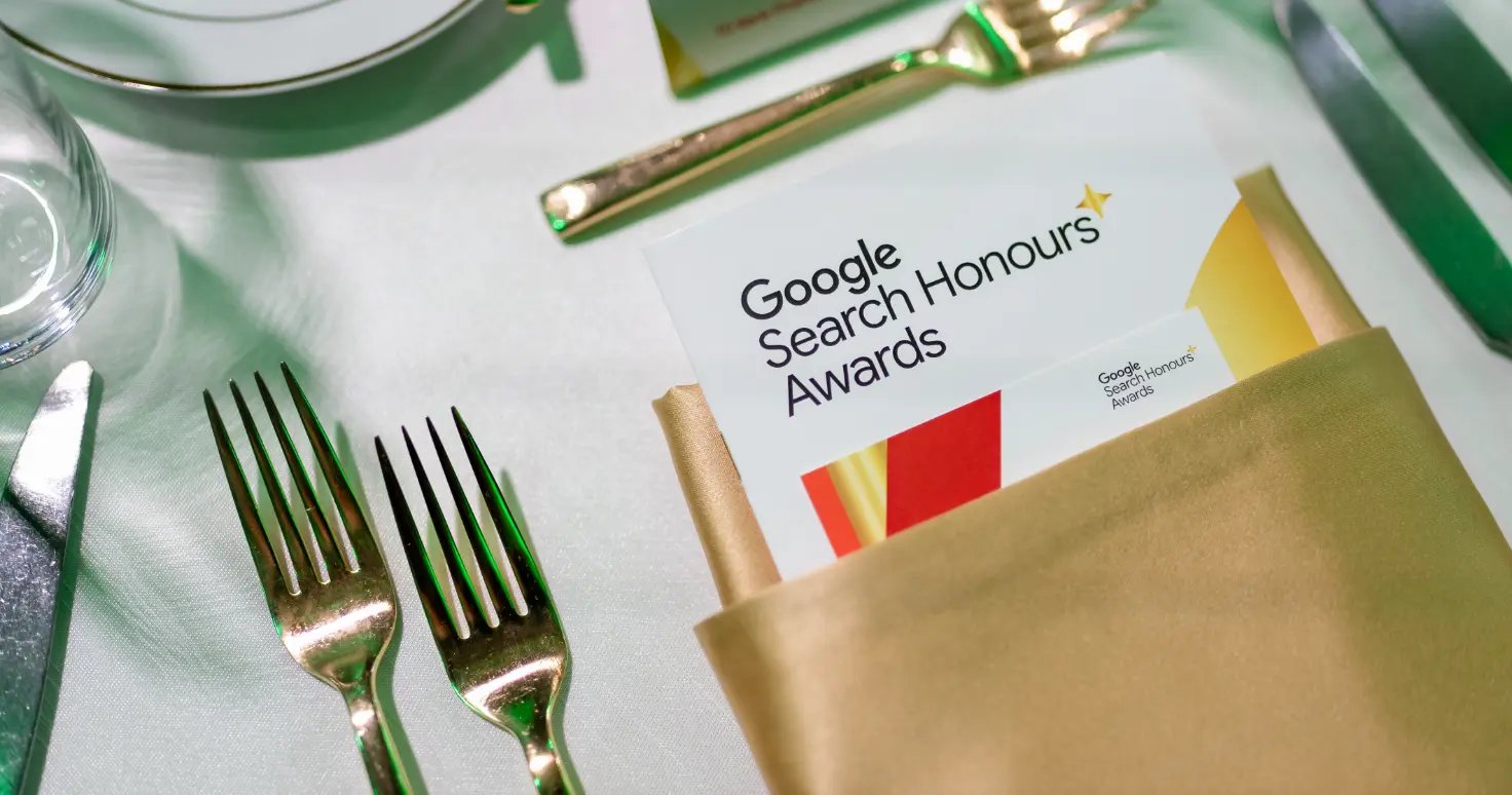 Un couvert de table avec des couverts et un programme intitulé « Google Search Honours Awards » dans une serviette dorée.