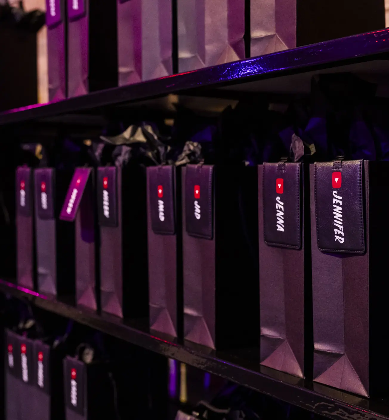 Rangées de sacs cadeaux violets avec des étiquettes de nom et le logo YouTube sur une étagère.