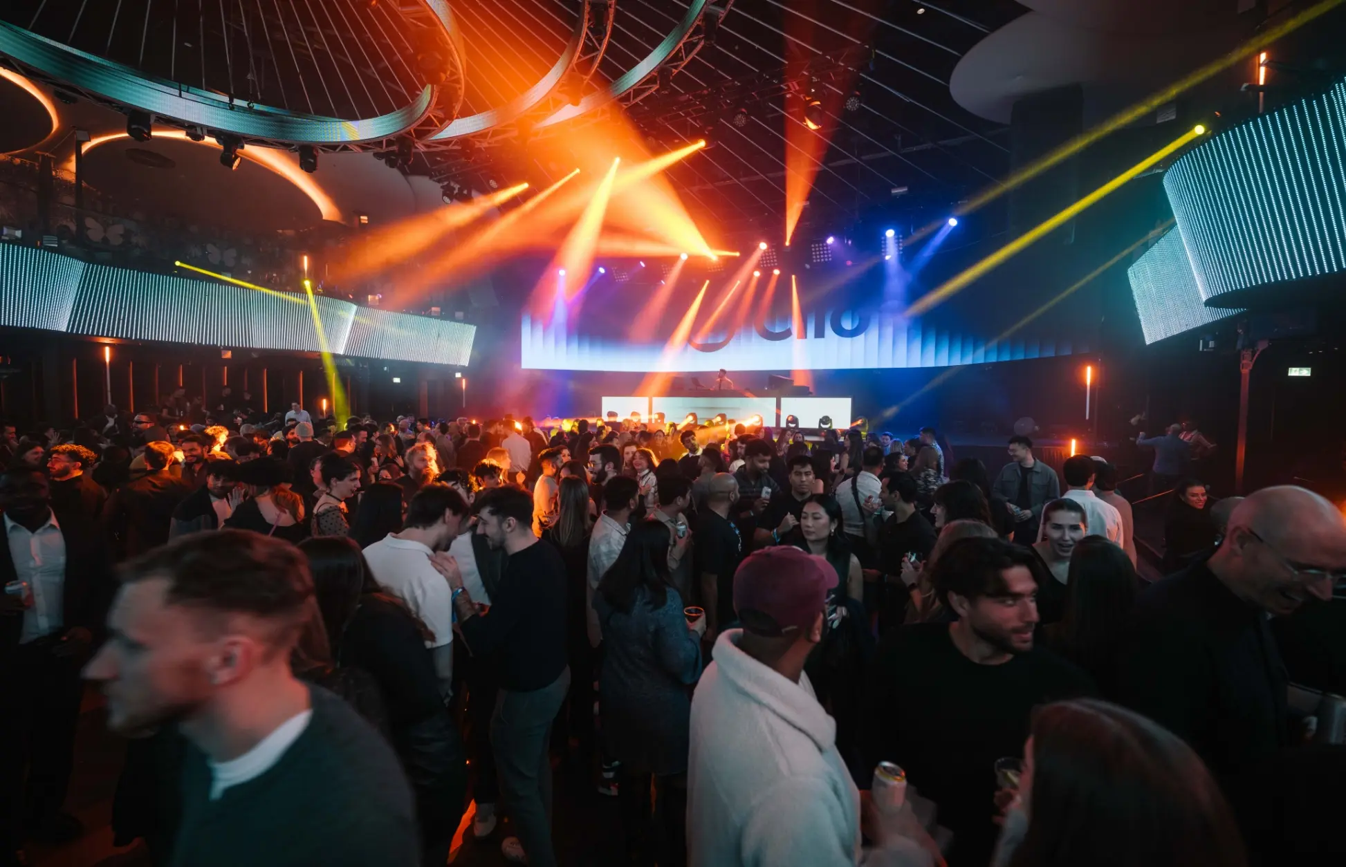 Une boîte de nuit bondée avec des lumières colorées et un DJ jouant de la musique.