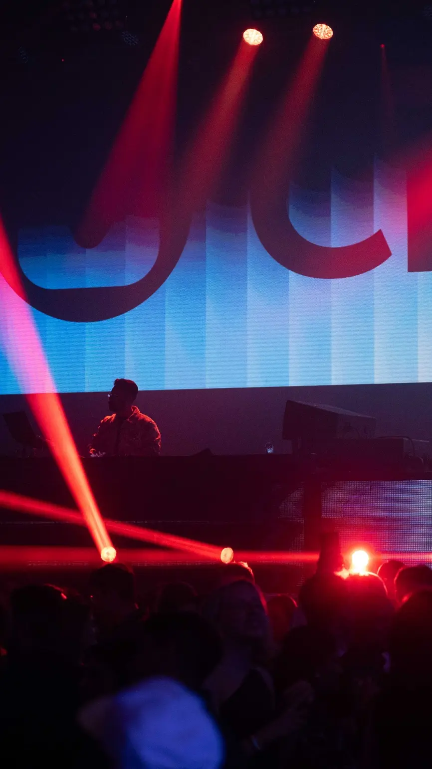 Un DJ se produisant sur scène avec des lumières colorées et une foule dansant au premier plan.