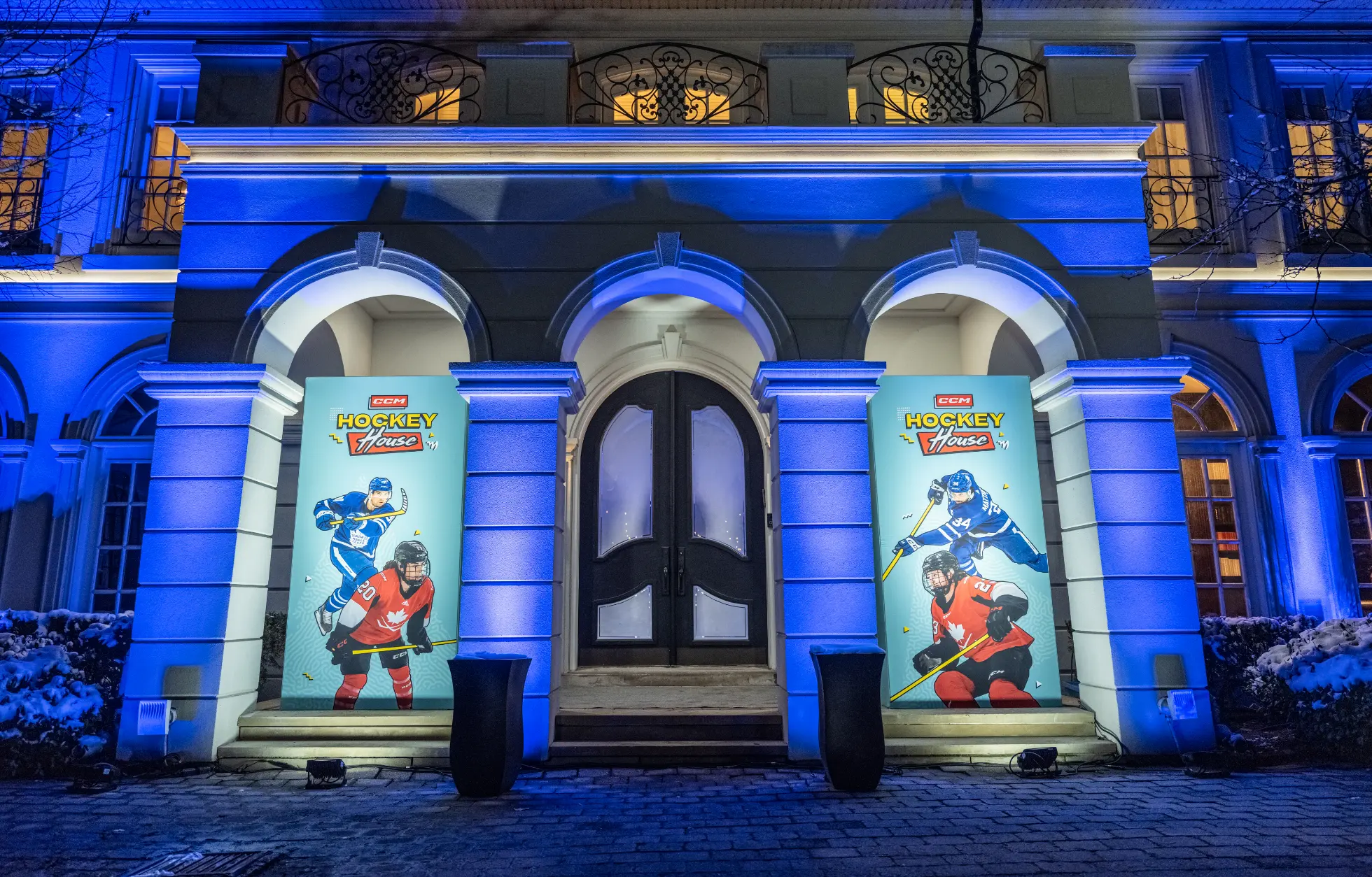 Une entrée de bâtiment illuminée en bleu avec des bannières présentant des joueurs de hockey de chaque côté.