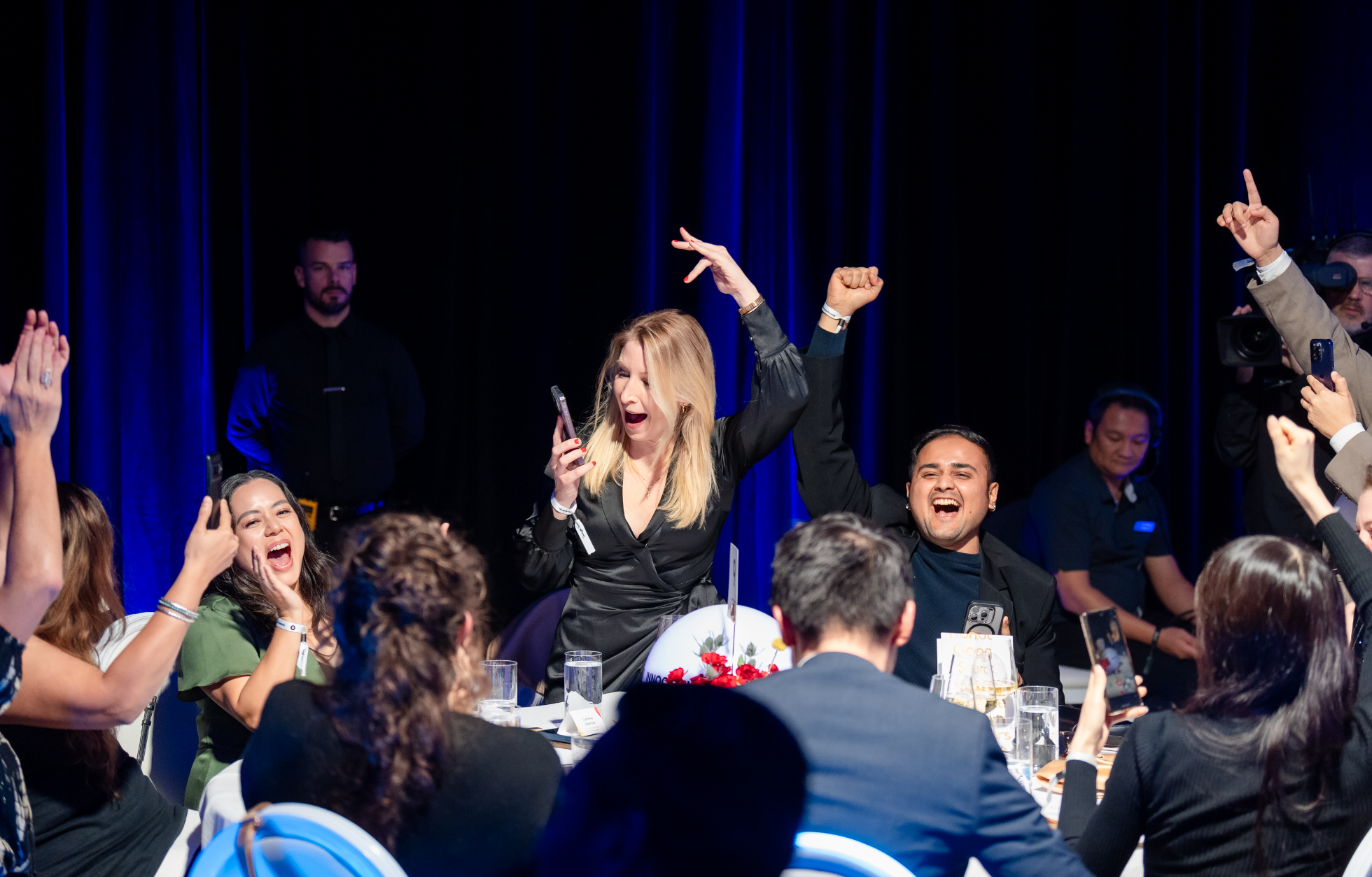Des personnes à une table applaudissent et célèbrent, certaines tenant leurs téléphones en l'air.