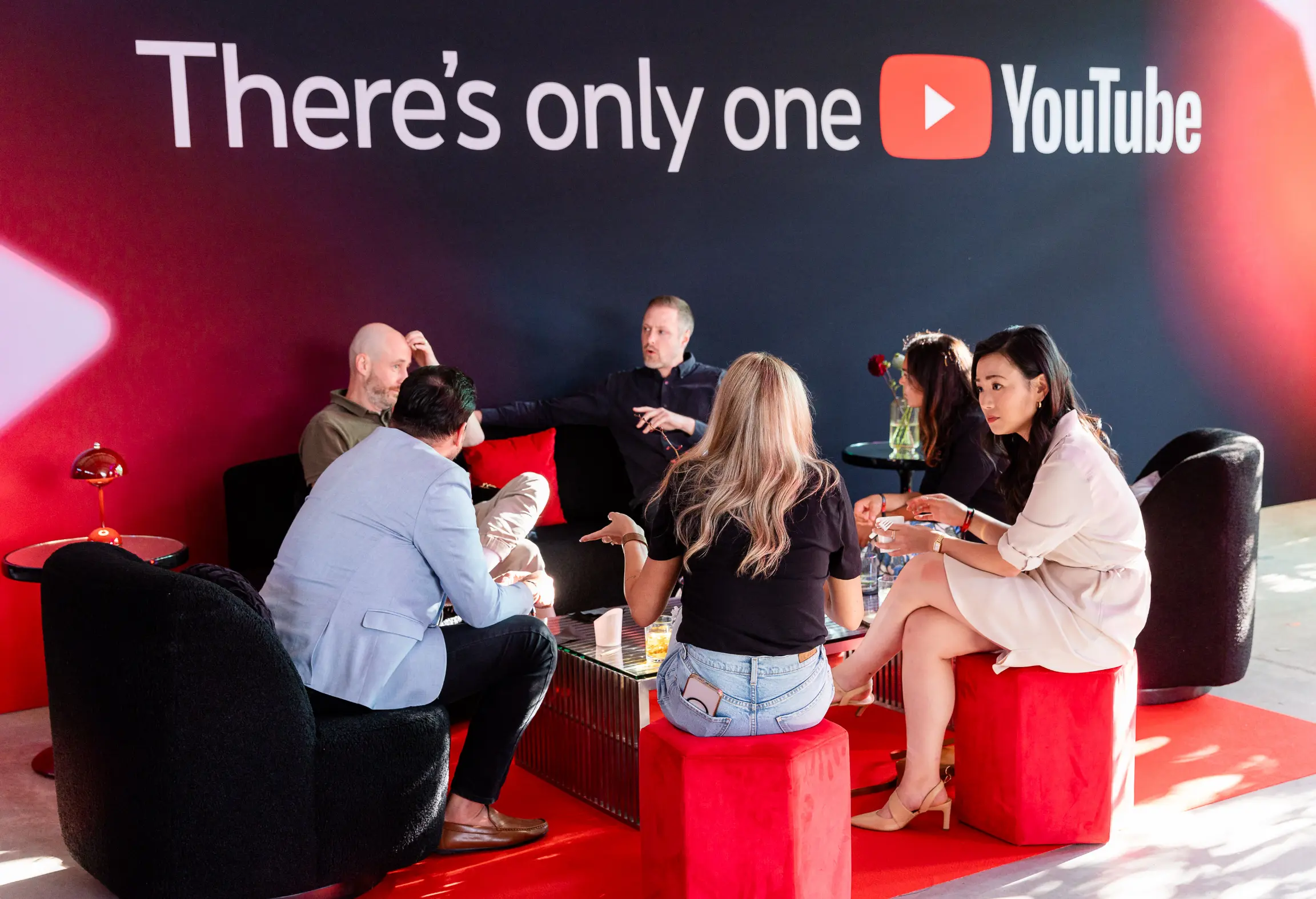 Un groupe de personnes assises et parlant dans un espace lounge avec un panneau YouTube en arrière-plan.