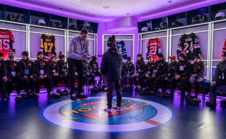 Un groupe d'enfants en vêtements d'hiver assis dans un vestiaire bien éclairé avec des maillots de hockey exposés.
