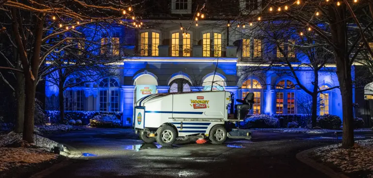 Une surfaceuse de glace illuminée garée devant un grand bâtiment éclairé la nuit.