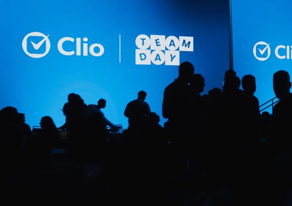 Foule en silhouette devant un écran bleu affichant "Clio Team Day."