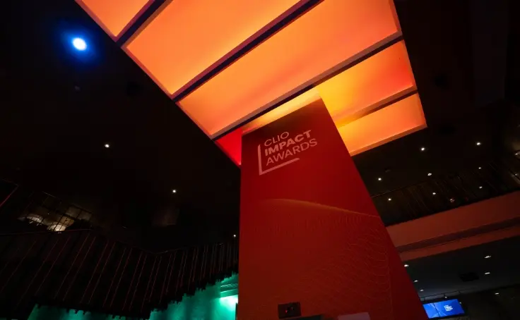A red and orange illuminated indoor space featuring a sign for the Clio Impact Awards.